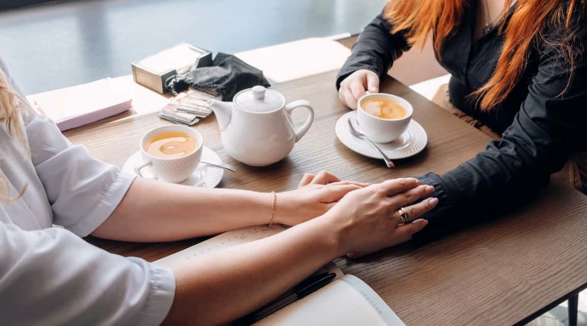 Dos mujeres tomando un café y cogiéndose de la mano en muestra de apoyo presencia parte de lo que es el coaching