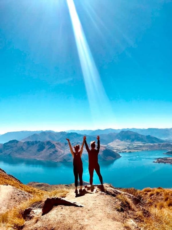 Dos personas en la cima de una montaña levantando los brazos al sol imagen de Coaching Emocional